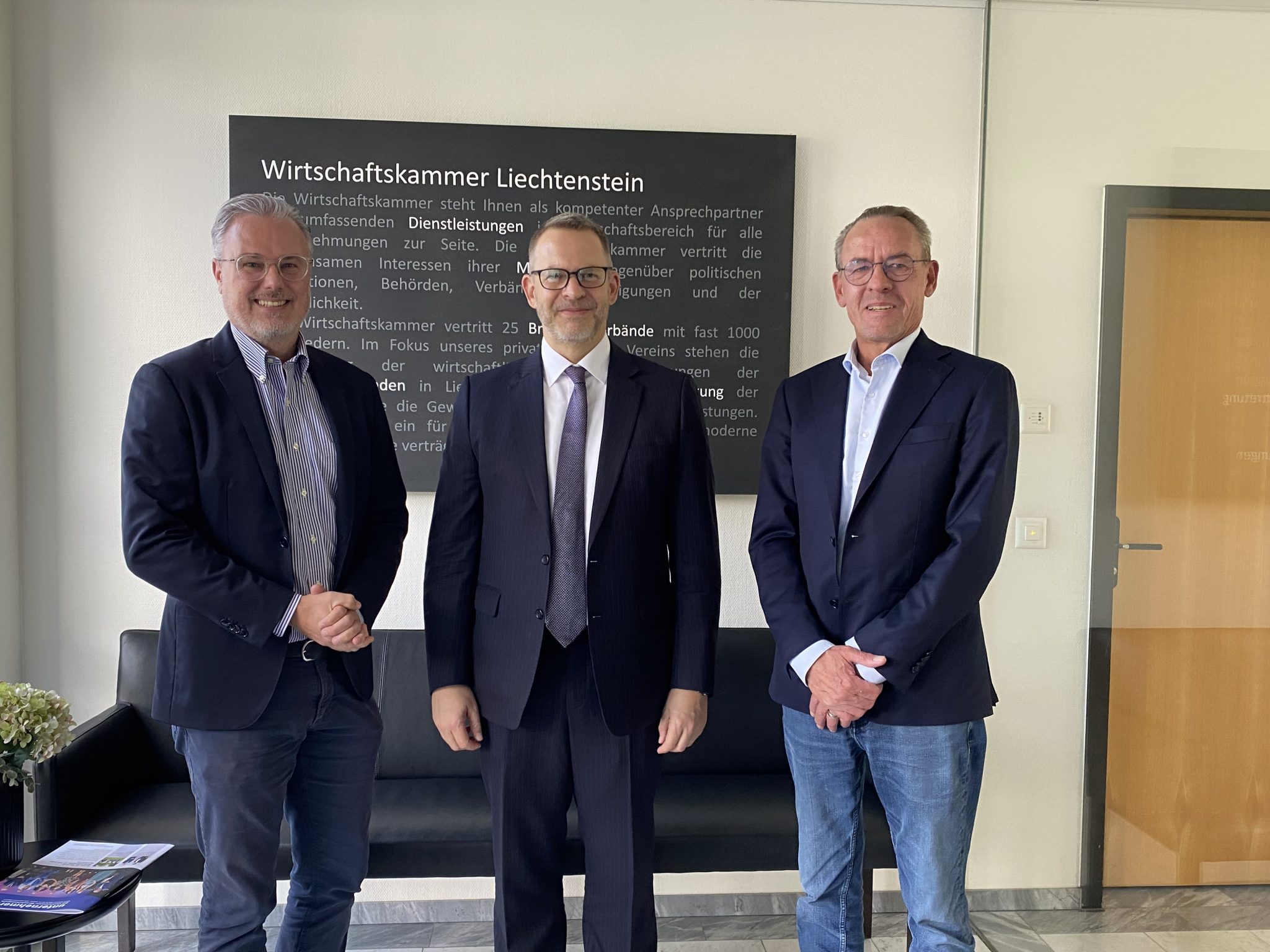 Drei Geschäftsmänner in moderner Büroumgebung bei der Diskussion im Wirtschaftskammer Liechtenstein.